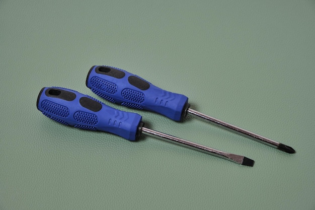 Two screwdrivers cross and flat with blue handles on a green background.