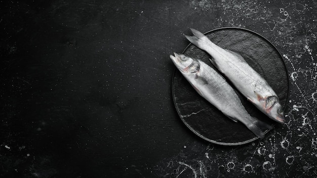 Two sea bass fish with spices on a black stone plate On a dark background Top view