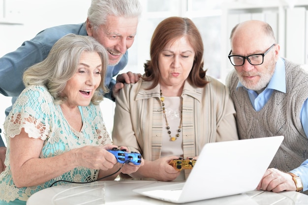 Two senior couples sitting at table and playing computer game