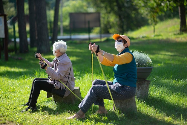 Two senior elderly women with face masks rest after a nordic walking during covid-19 pandemic