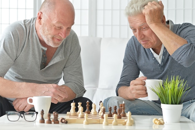 Two senior men having fun and playing chess at home