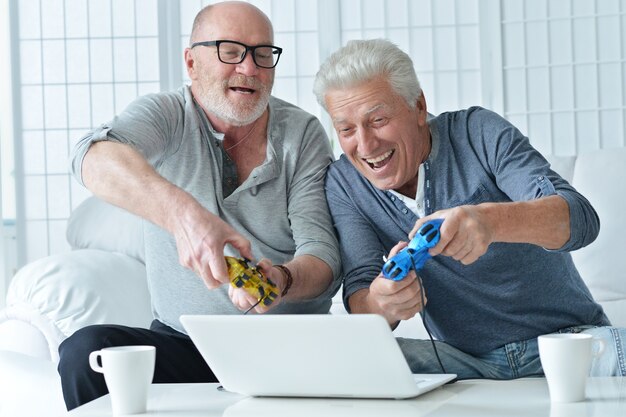 Two senior men having fun and playing on laptop at home