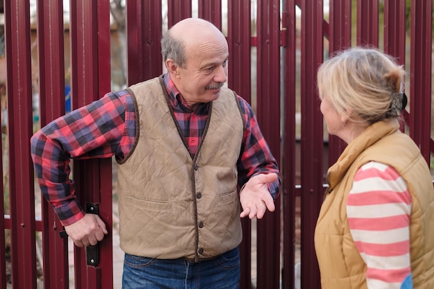 two senior neighbors takling to each other on sunny day near fence