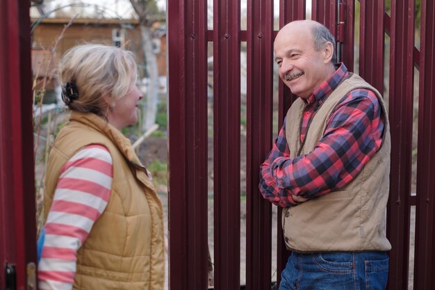 Two senior neighbors takling to each other on sunny day near fence