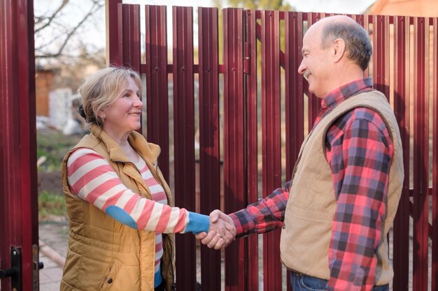 two senior neighbors takling to each other on sunny day near fence