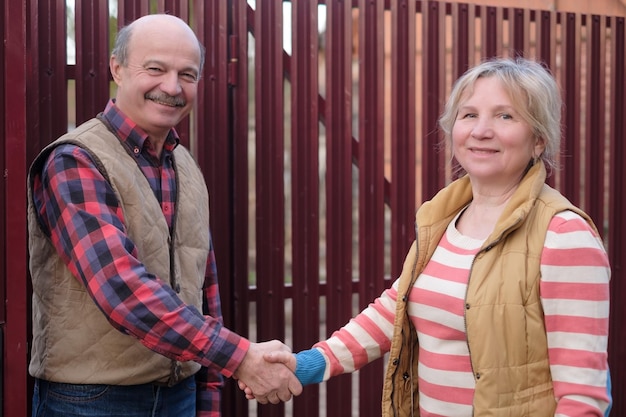 Two senior neighbors takling to each other on sunny day near fence