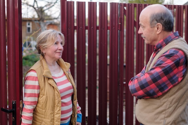 two senior neighbors takling to each other on sunny day near fence