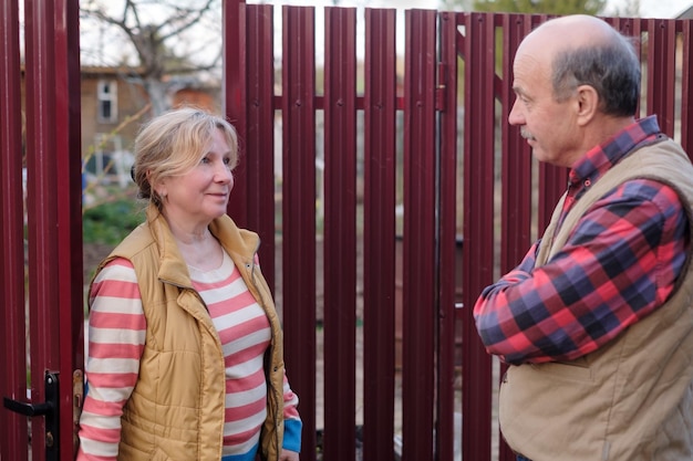 Two senior neighbors takling to each other on sunny day near fence