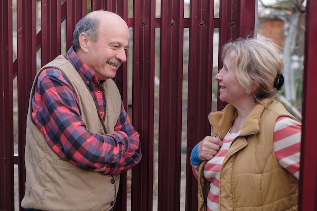 two senior neighbors takling to each other on sunny day near fence