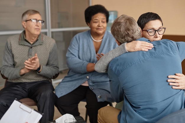 Two senior people embracing in group therapy session
