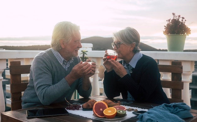 Двое пожилых людей наслаждаются завтраком на террасе на рассвете Фон гор