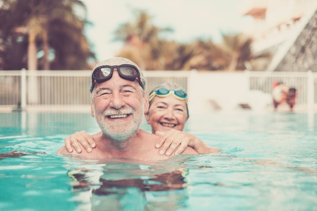 Due anziani in piscina abbracciati e giocando - persone mature felici e un paio di pensionati che guardano la telecamera sorridendo