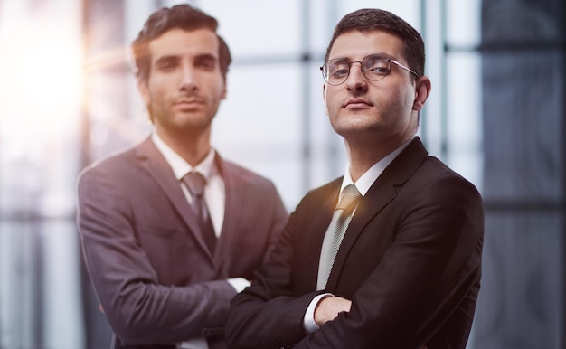 Two serious young businessmen standing with arms crossed in office