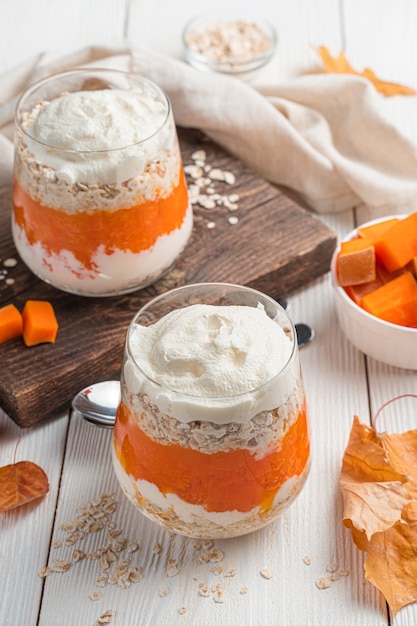 Two servings of pumpkin parfait with cream and cereals on a white background