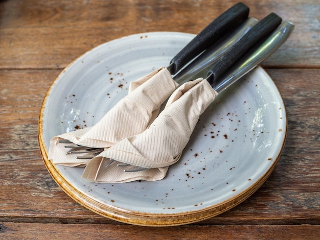 Two set of clean fork and knife wrapped in tissue napkin in the ceramic dish