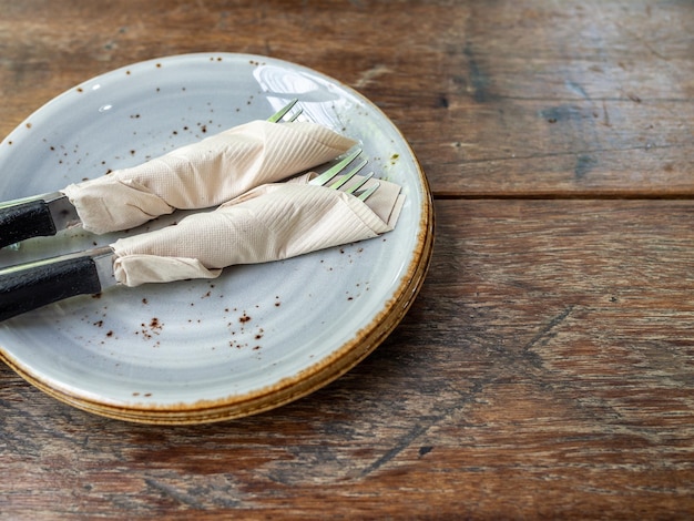 Two set of clean fork and knife wrapped in tissue napkin in the ceramic dish