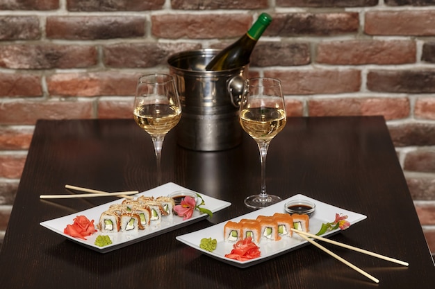 Two sets of sushi rolls with chopsticks and wine glasses