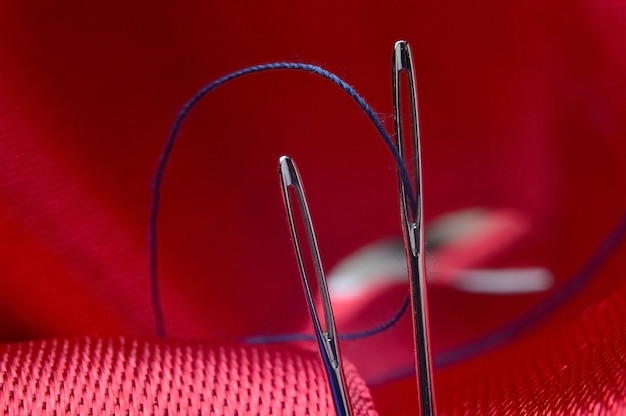 Two sewing needles with blue thread on a background of red fabric. close-up.