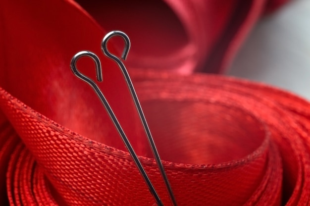 Two sewing pins on the background of a red cloth tape. close-up.