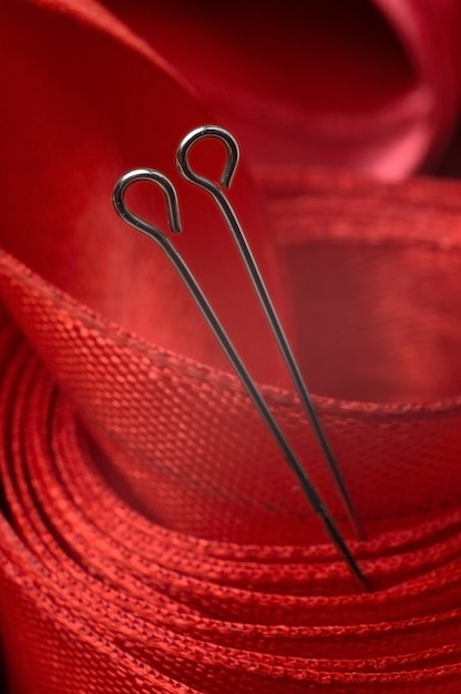 Two sewing pins on the background of a red cloth tape. close-up.