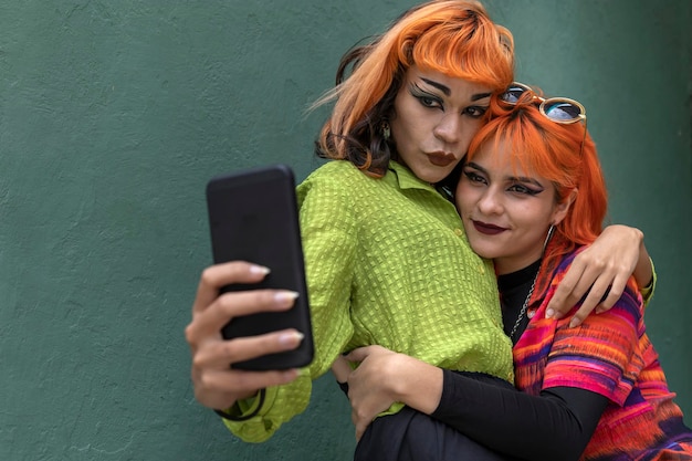 성적으로 다양한 라틴계 친구 두 명이 서서 휴대전화로 사진을 찍고 있다