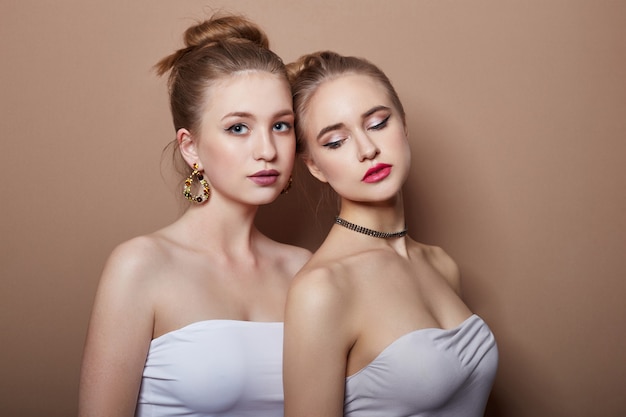 Two sexy fashion young blonde girls hugging, perfect hair, earrings in ears jewelry on neck, beautiful eyes