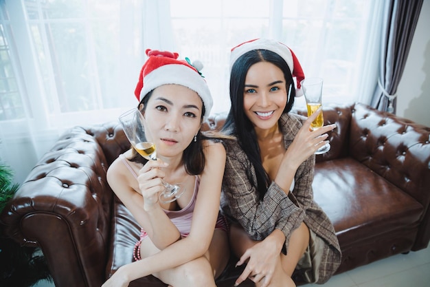 Two sexy women wear red santa hat celebrate Christmas party together with drink wine in the home.