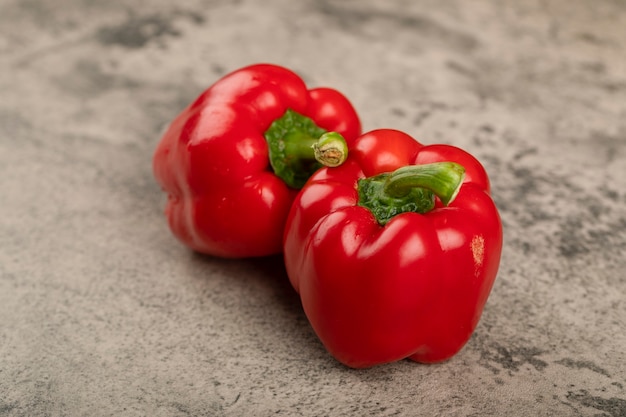 Two shiny red bell peppers on stone surface