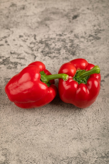 Two shiny red bell peppers on stone surface