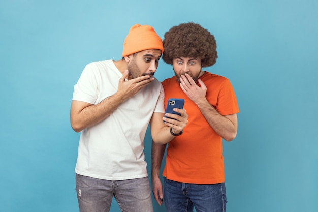 Two shocked men standing using smartphone reading breaking news in social networks