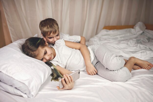 Two siblings watching video in mobile electronic device in the bed, gadget addiction