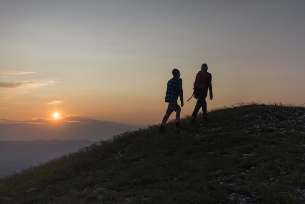 Foto due silhouette maschio e femmina che conquistano una vetta di montagna dando un alto cinque e godendosi il