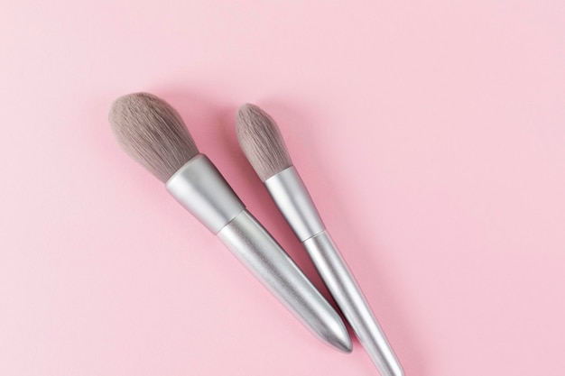 Two silver color professional makeup brushes on pink colored background Creative concept of beauty Copy space Flat lay