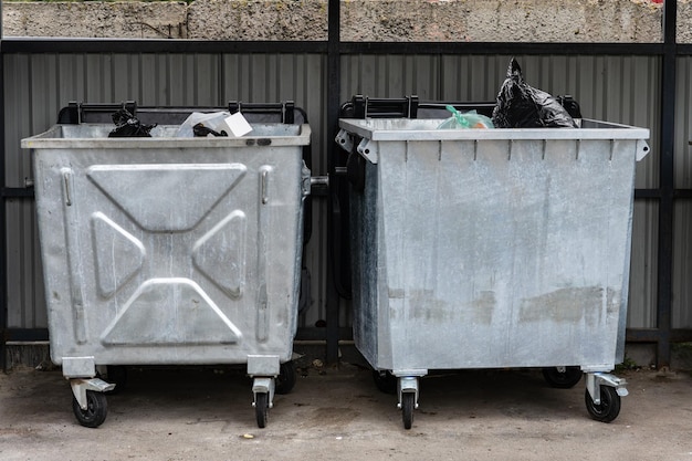 黒いプラスチック袋で満たされた車輪に置かれた2つの銀のゴミ容器