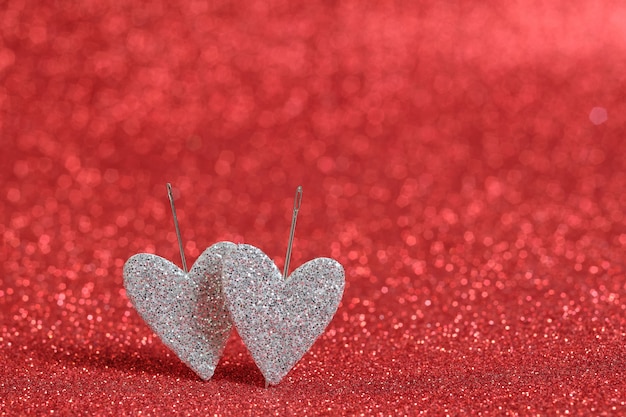 Two silver hearts on a red bokeh wall. Hearts are pierced to the wall with needles. Picture for Valentine's Day and wedding. Bokeh red color wall.