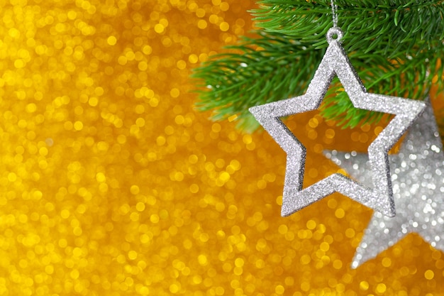 Two silver star on a Christmas tree branch on a yellow shining background from bokeh