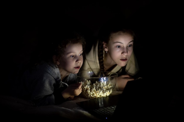 Two sister girls watch cartoons on the device and have a fun\
together childhood leisure