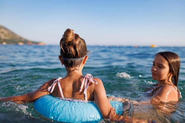 Two sisters in bathing suits play with an inflatable ring in the sea