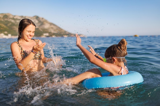 Two sisters in bathing suits play with an inflatable ring in the sea