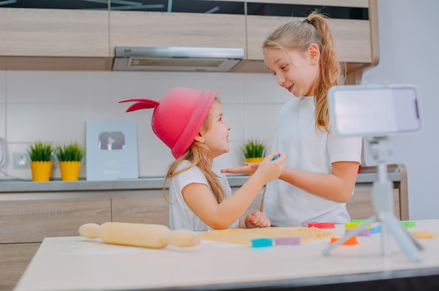 Two sisters bloggers are preparing cookies in the kitchen and filming a culinary video on a smartphone.