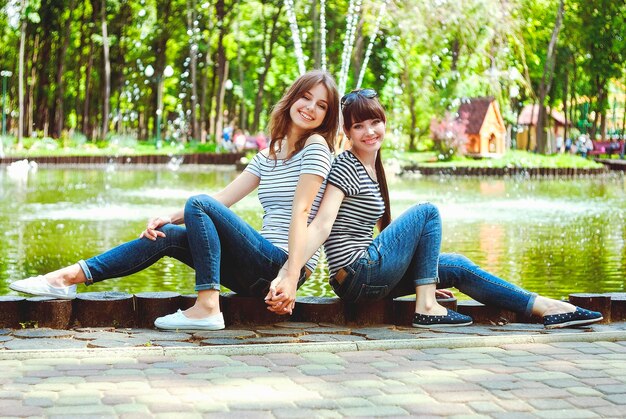 Two sisters, friends have fun, laugh, eat cotton candy, walk in a summer green amusement park. Happy