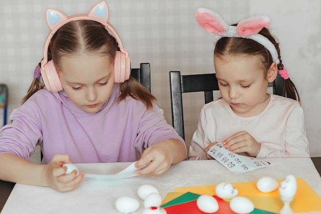 Two sisters at home at the table stick stickers on eggs