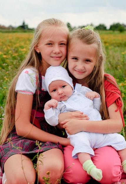 Two sisters hug one another and baby brother outdoors, happy family