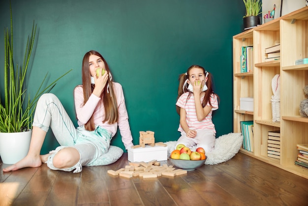 Two sisters in medical mask eating apple at home during covid quarantine.