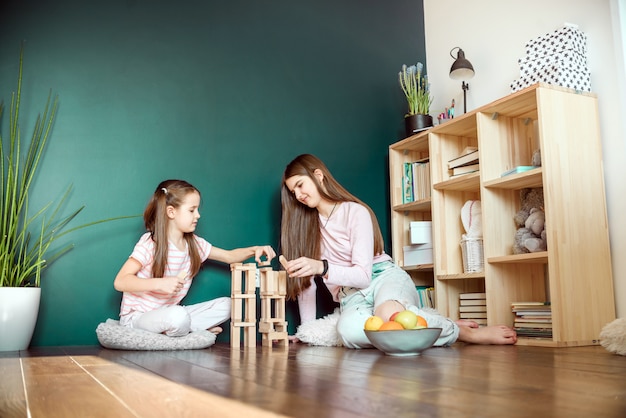 Two sisters in medical mask playing playing a blocks wood tower game