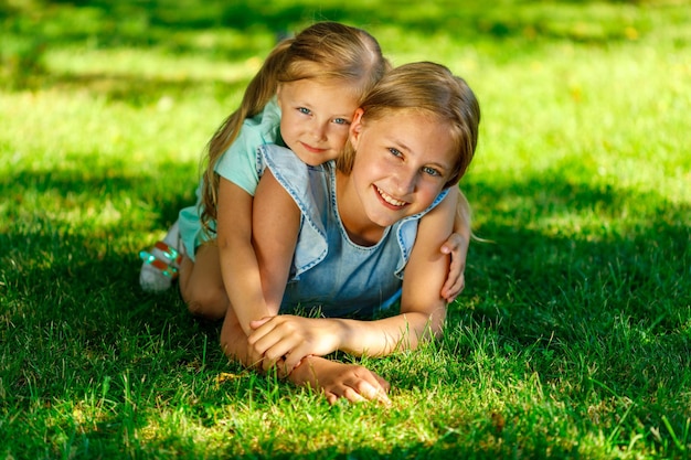 Two sisters in the park. the younger hugs the older one.