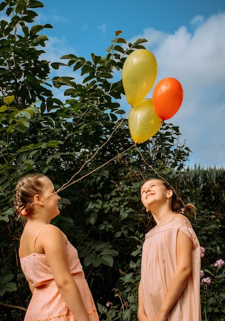 two sisters in pink dresses and with balls tied to their braided hair are standing outside
