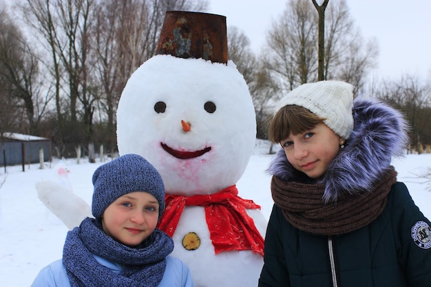 冬の日に雪だるまの近くで遊ぶ 2 人の姉妹 子供たちが雪だるまを作る 2 人の姉妹が冬の日に雪だるまを作る