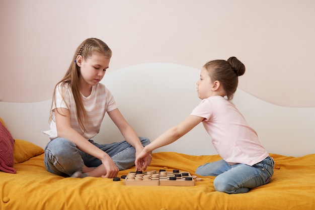 Two sisters playing checkers on a bad having fun at home, happy children concept