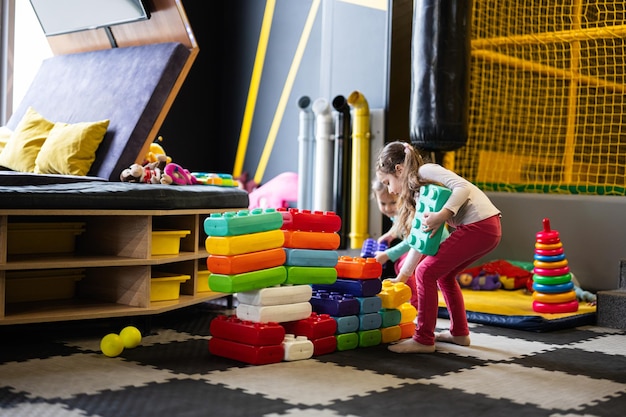 Two sisters playing at kids play center while build with colored plastic blocks